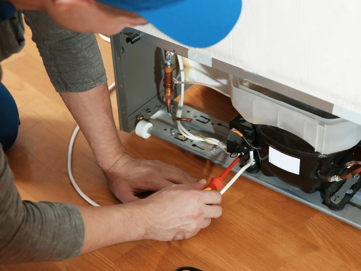 A technician repairing a refrigerator in a Kingsburgh kitchen.